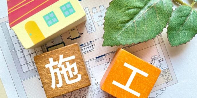 設計図の上に置かれた家の模型と『施工』の文字が書かれた積み木