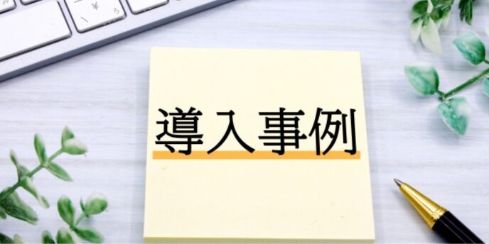 「導入事例」と書かれた付箋とパソコン、観葉植物のあるデスク風景