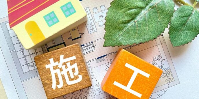 住宅模型と設計図の上に置かれた『施工』の文字ブロックと緑の葉が並ぶイメージ