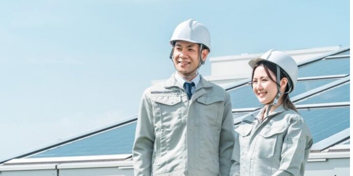 太陽光パネルの前で笑顔を見せる作業着姿の男性と女性作業員