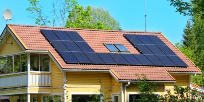 赤い屋根に太陽光パネルを多数設置した黄色い住宅と晴れた空
