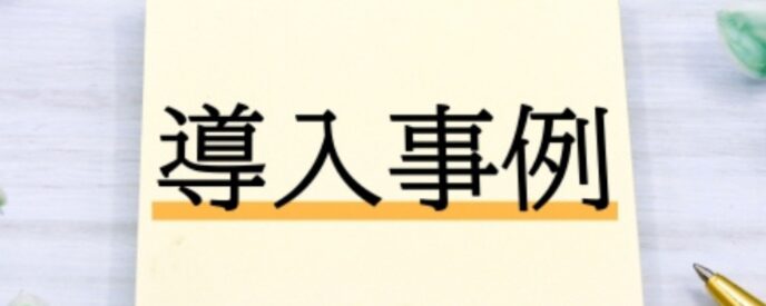 『導入事例』と書かれた付箋メモとキーボード、観葉植物、ボールペンが並ぶデスクの上
