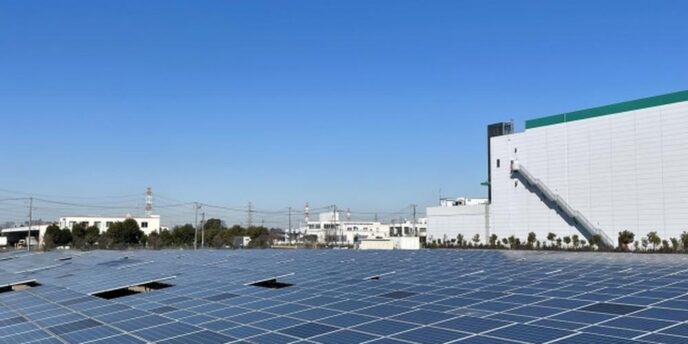 青空の下、工場の隣に広がる大規模な太陽光発電パネル群