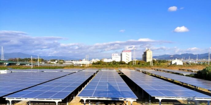 晴天の下に広がる太陽光発電パネルとその奥に見える都市の風景