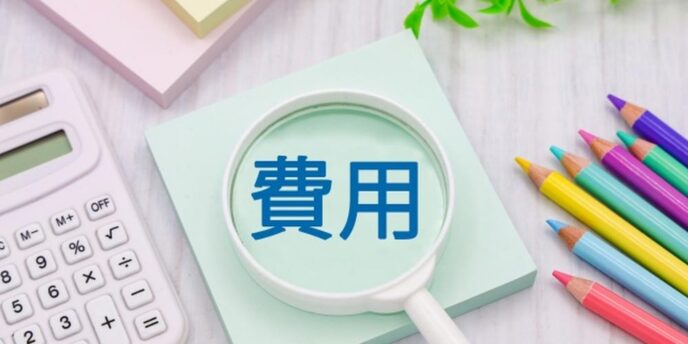 虫眼鏡で強調された『費用』の文字と電卓、色鉛筆が並ぶイメージ