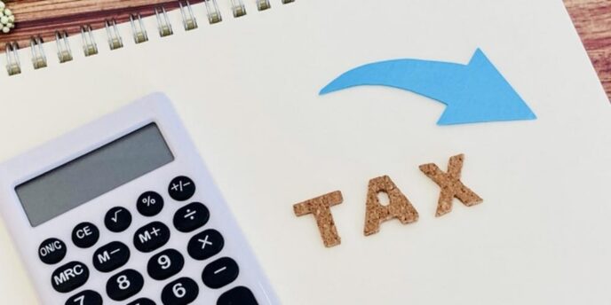 ノートの上に置かれた電卓と「TAX」の文字、青い矢印が添えられた節税のイメージ。