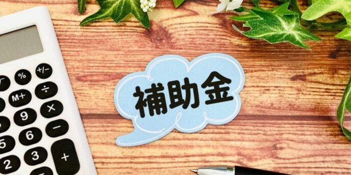 補助金と書かれた吹き出し、電卓とペンが並ぶ資金サポートのイメージ