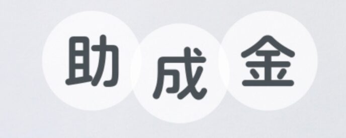 白背景に浮かぶ『助成金』の文字とカラフルな用紙。補助金制度や支援金の案内を示すビジュアル