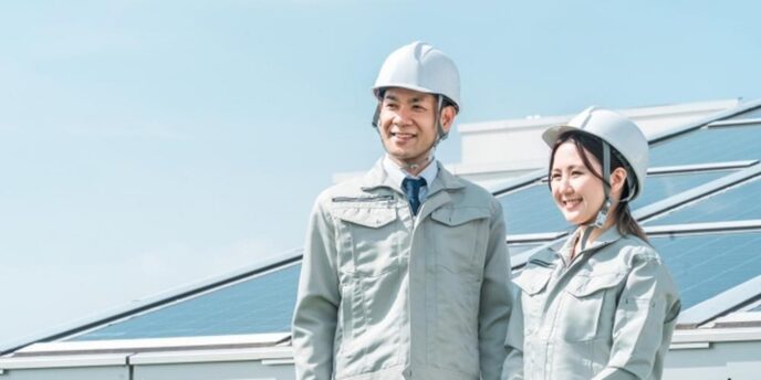 太陽光パネルの前で笑顔を見せる作業服姿の男性と女性スタッフ