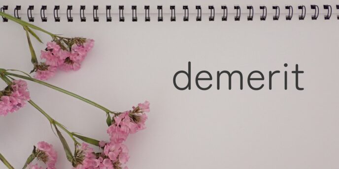 ノートに綴られた「demerit」の文字とピンクの花、ペンのある構図