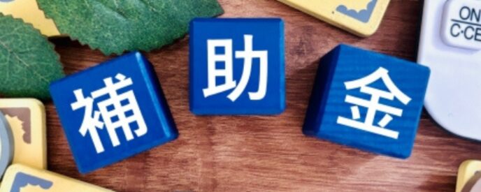補助金と書かれた青いブロックと紙幣・硬貨風のプレート、資金支援を表すイメージ