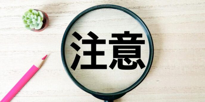 虫眼鏡で強調された『注意』の文字と卓上の文具のイメージ