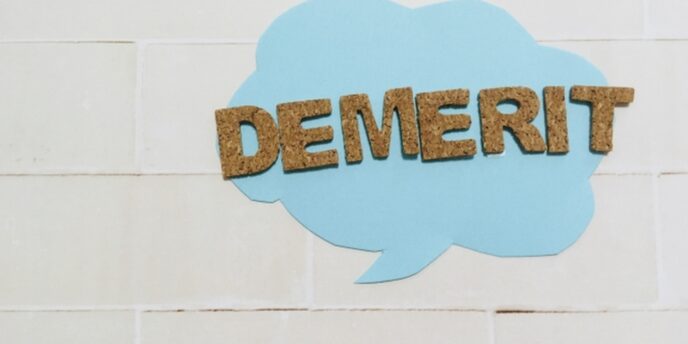 青い吹き出しに貼られた『DEMERIT』のコルク文字。注意点や欠点を伝えるイメージ