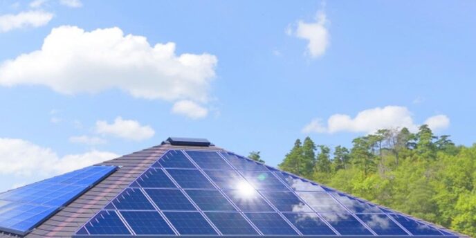 一戸建て住宅の屋根に設置されたソーラーパネルが青空の下で光っている様子。